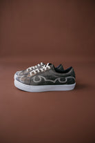 Western-inspired brown sneakers with decorative stitching and white soles on brown background