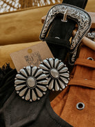 Western concho earrings with floral design, silver engraved belt, suede jacket detail.