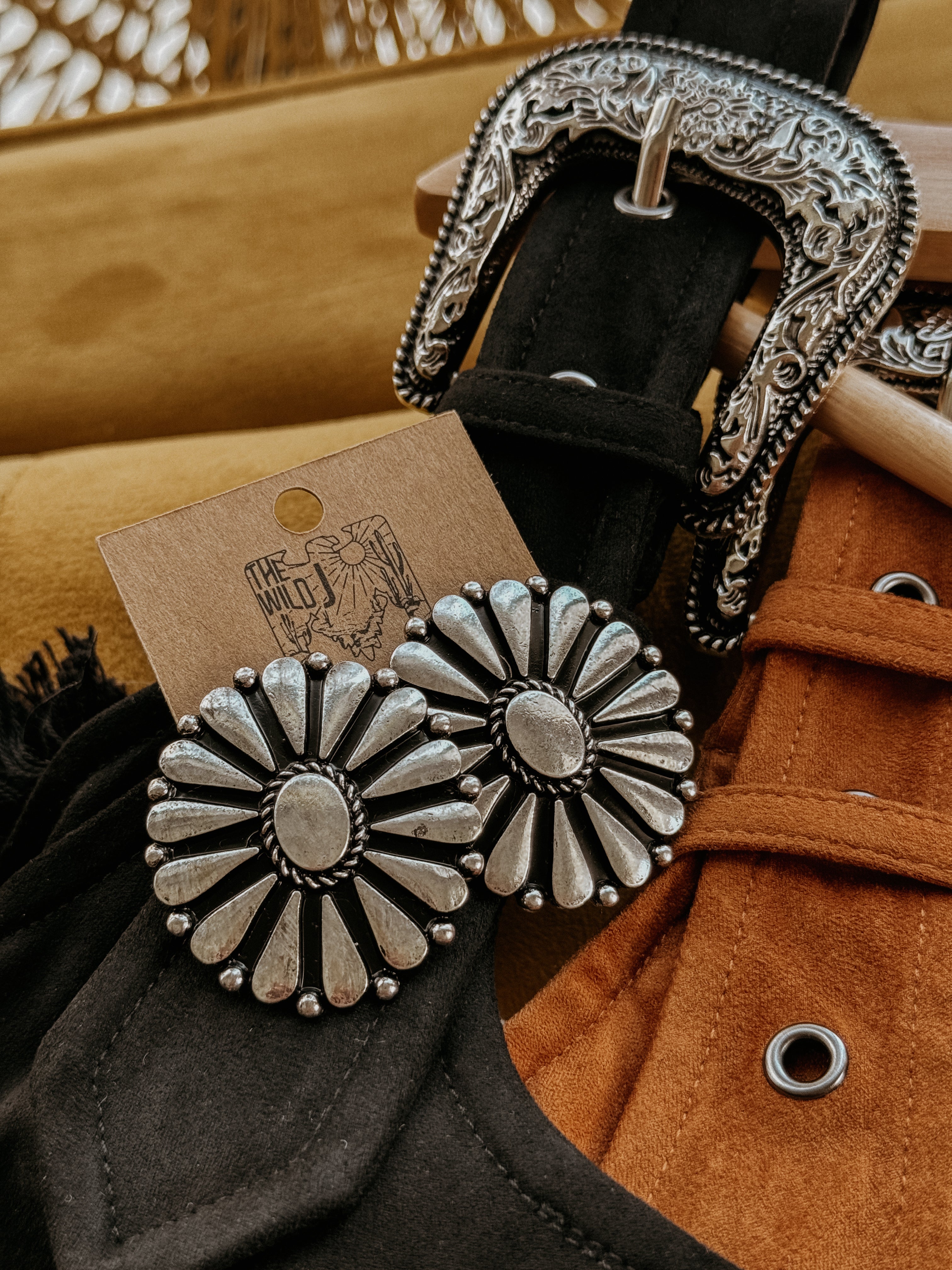 Western concho earrings with floral design, silver engraved belt, suede jacket detail.