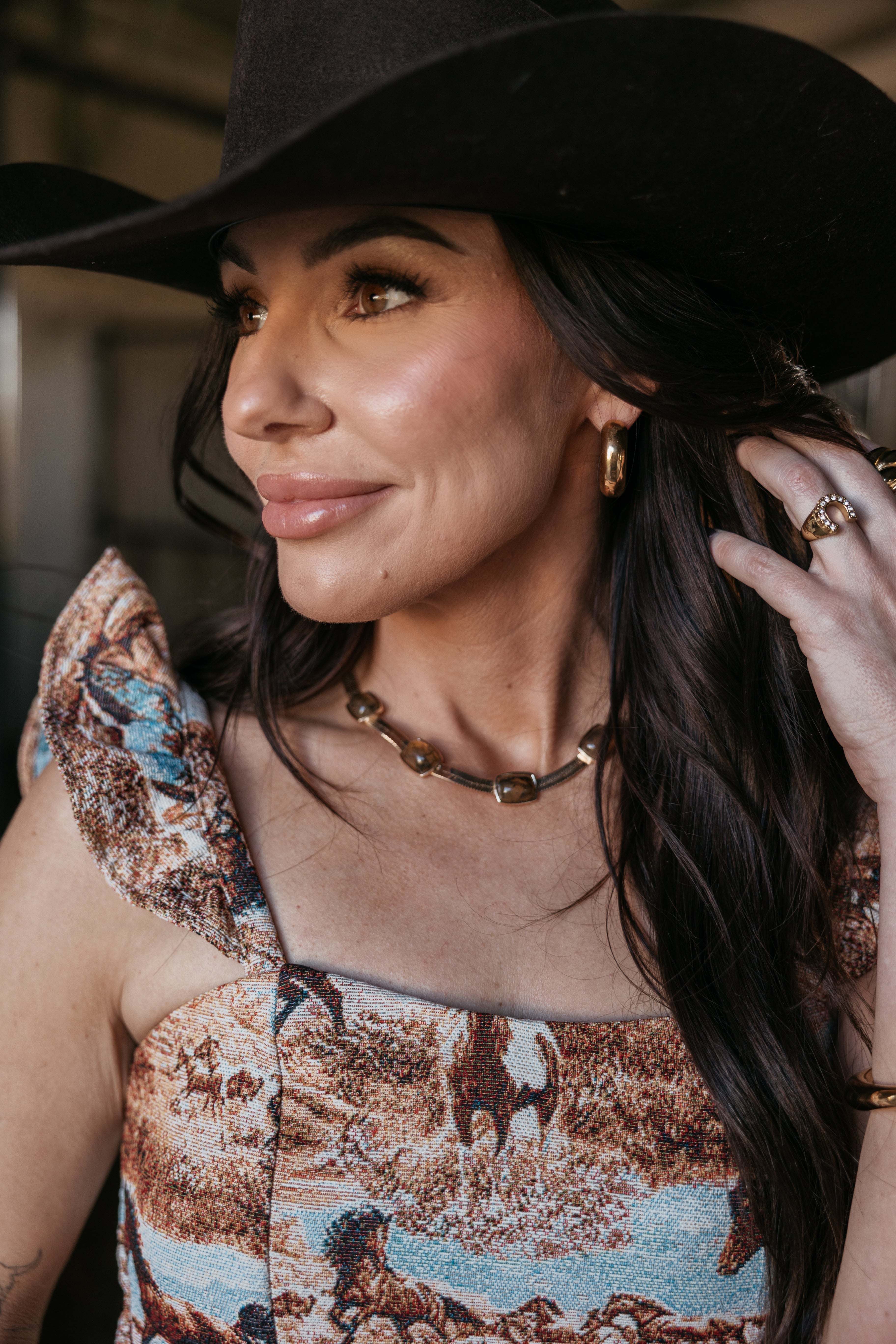 Woman in western boho dress with horse print, wearing a black cowboy hat and gold jewelry