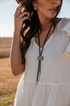 Woman in white western boho dress with concho earrings and silver bolo tie outdoors