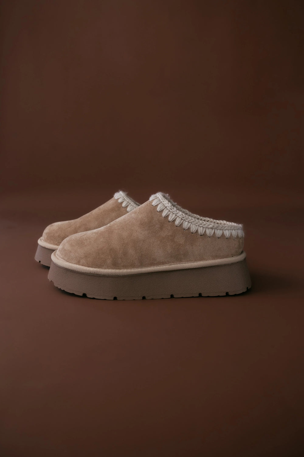 Pair of beige slippers with white trim on a brown background