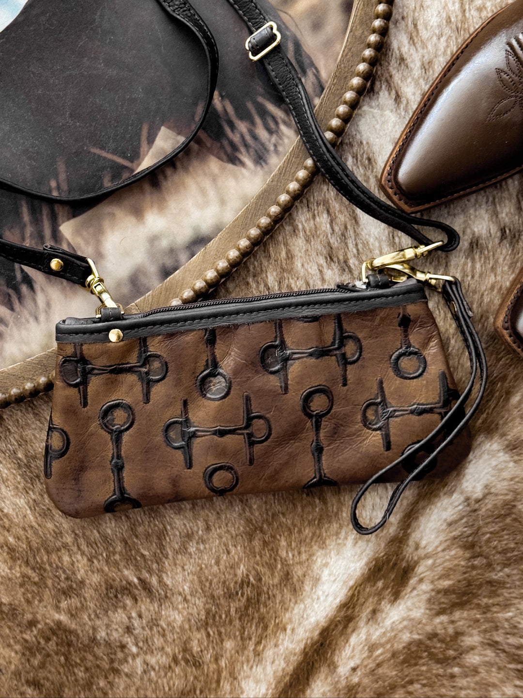 Caramel leather clutch with embossed horse-bit pattern and chocolate trim on western backdrop.