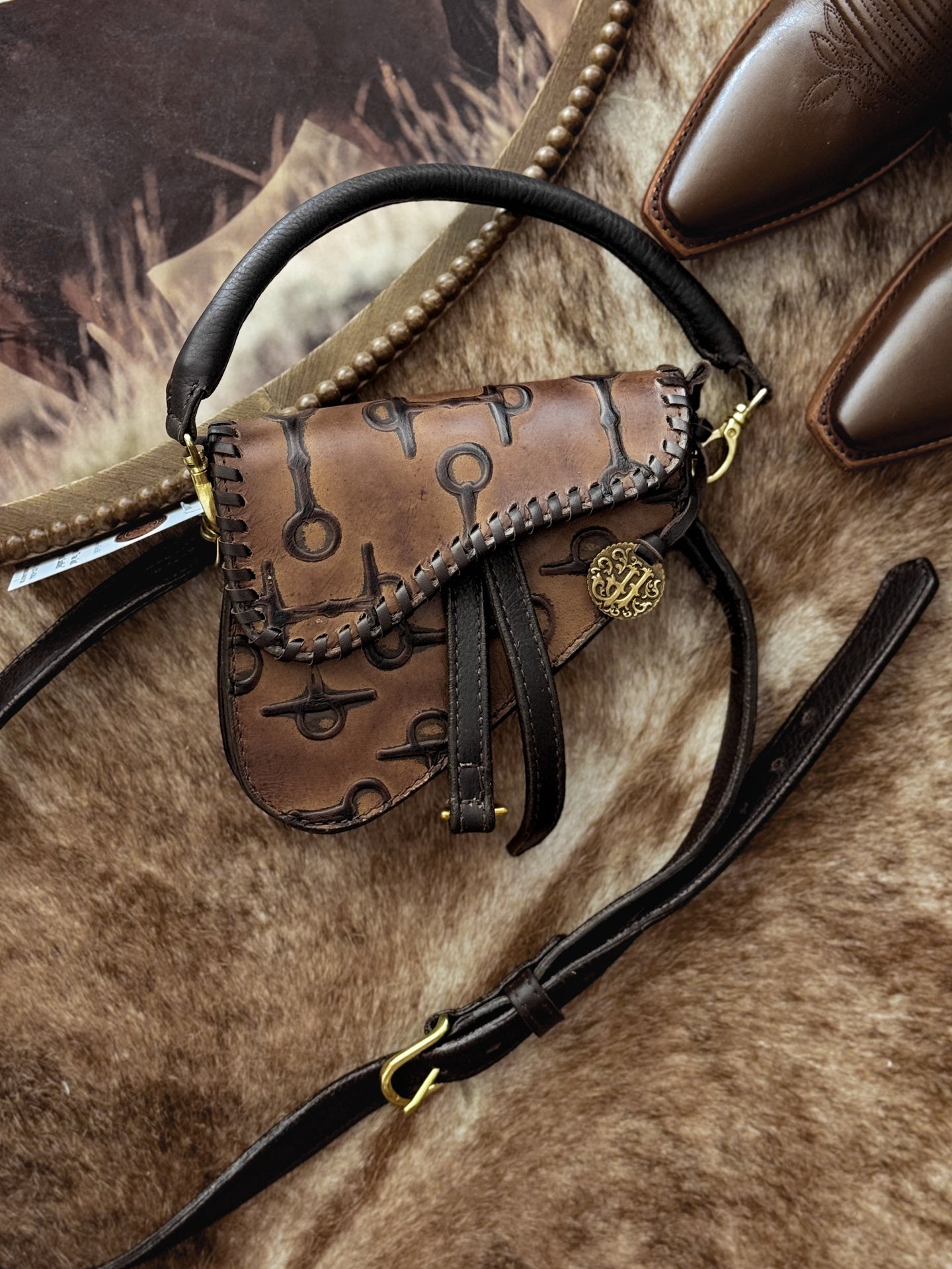 Caramel embossed leather saddle-style purse with snaffle-bit pattern and gold hardware.