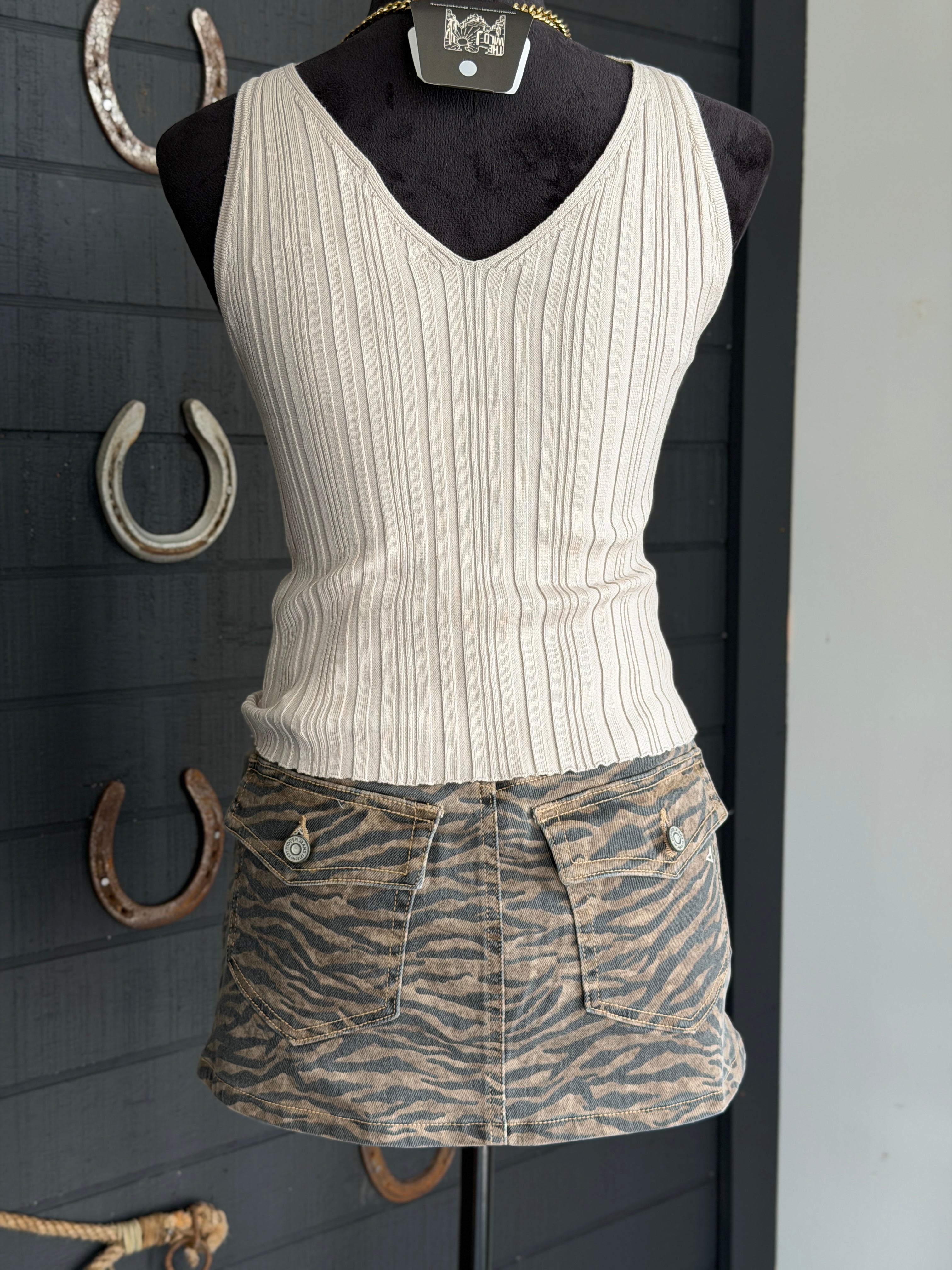 White ribbed tank top and zebra print shorts on a mannequin against a dark background with horseshoes.