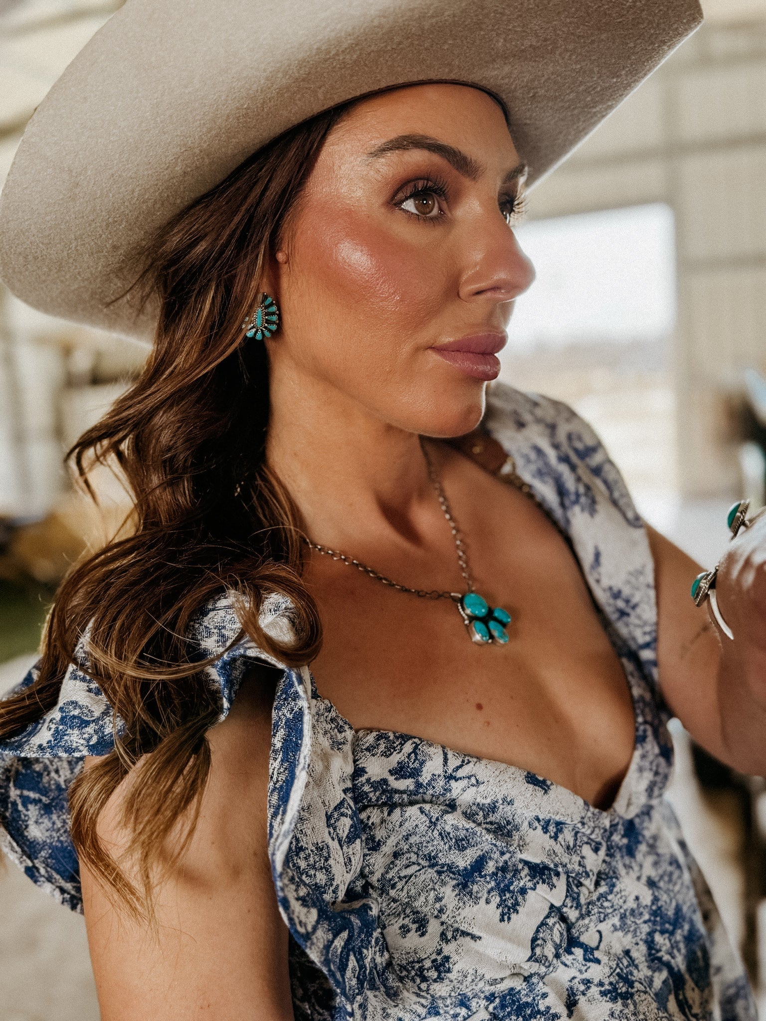 Woman in a cream cowboy hat wearing turquoise western jewelry and blue floral dress