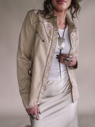 Woman wearing western embroidered tan jacket, white tank top, cream satin skirt, statement jewelry