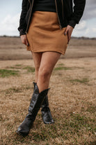 Woman wearing tan mini skirt and black western cowboy boots in a rustic outdoor setting