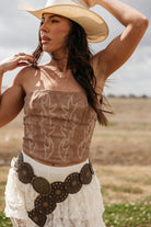 Woman in cowgirl hat, embroidered suede corset top, lace skirt, and western concho belt outdoors