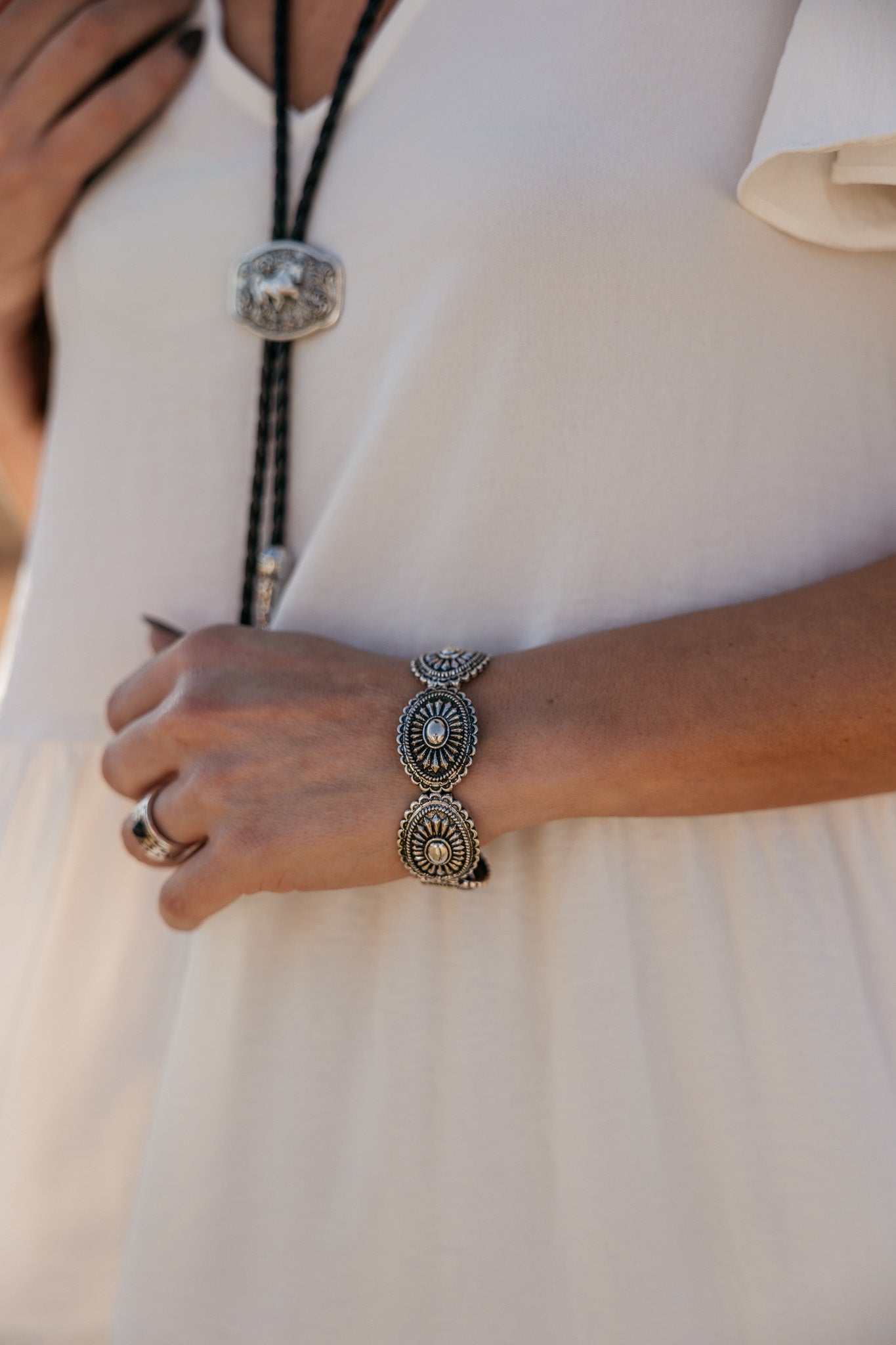 Woman wearing western concho bracelet, bolo tie necklace, and cream boho dress