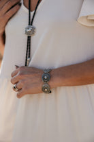 Woman wearing western concho bracelet, bolo tie necklace, and cream boho dress