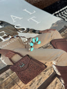 Turquoise western ring on magazine with cowgirl outfit, tooled leather bag, and cowboy boots.
