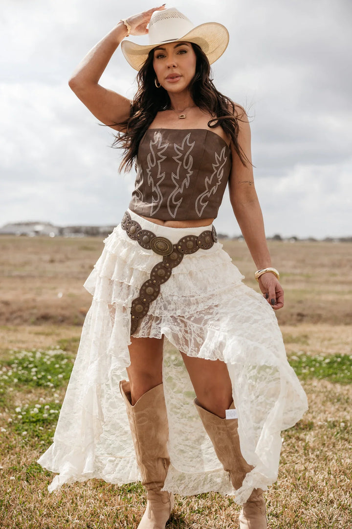 Woman in western boho outfit with cowboy hat, brown corset top, lace skirt, and boots outdoors
