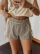 Person wearing a beige top with floral design and checkered shorts, holding a phone.