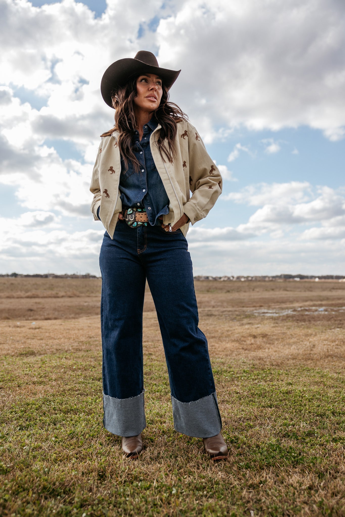 Woman in cowgirl hat, western jacket, denim shirt, wide-leg jeans and boots outdoors