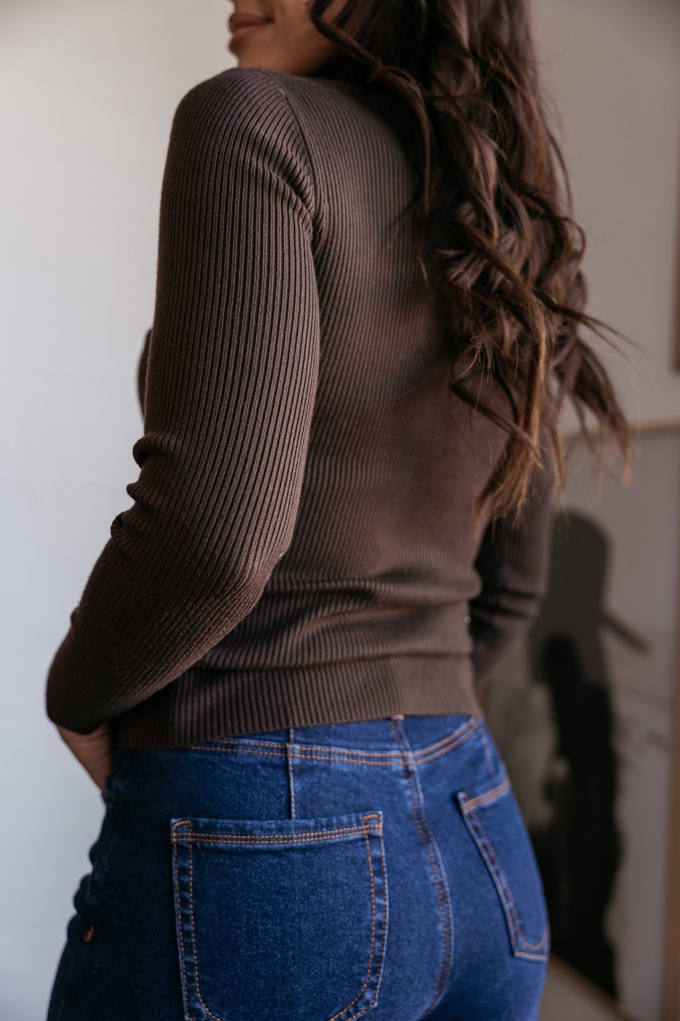 Woman wearing a brown ribbed sweater and high-waisted blue jeans, western casual style
