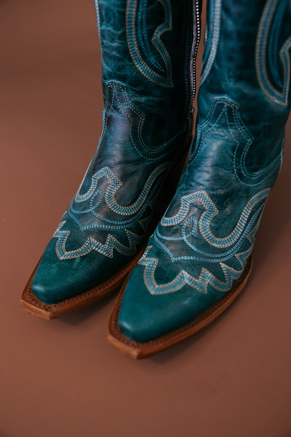 Turquoise leather cowgirl boots with intricate western stitching on brown background