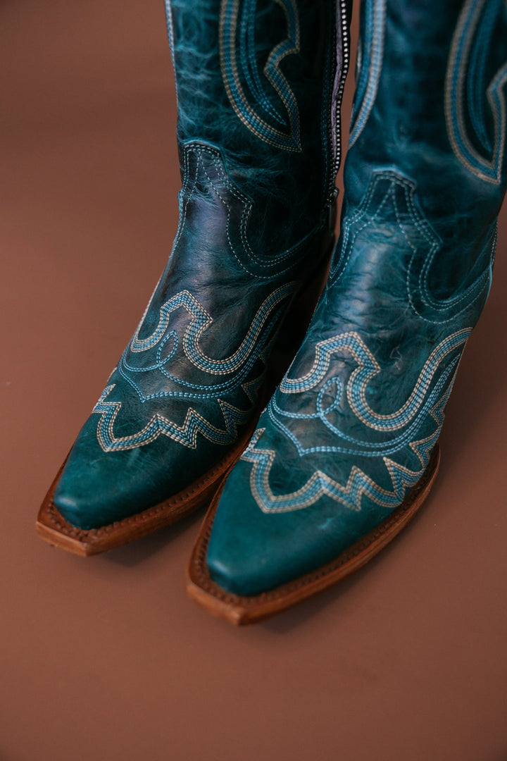 Turquoise leather cowgirl boots with intricate western stitching on brown background