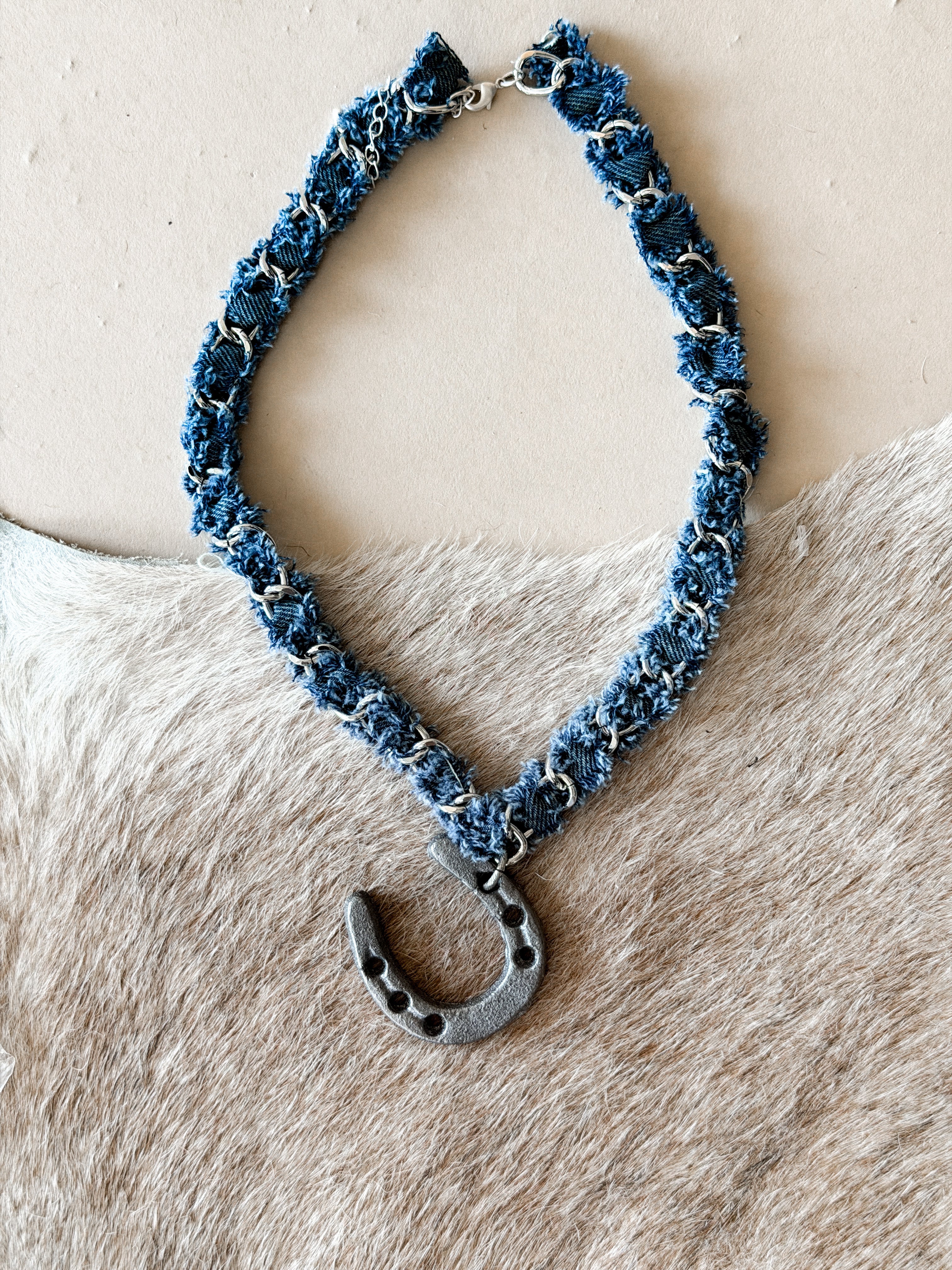 Western boho denim choker necklace with metal horseshoe pendant on cowhide background