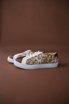 Brown and white cow print western sneakers with white soles on a brown background