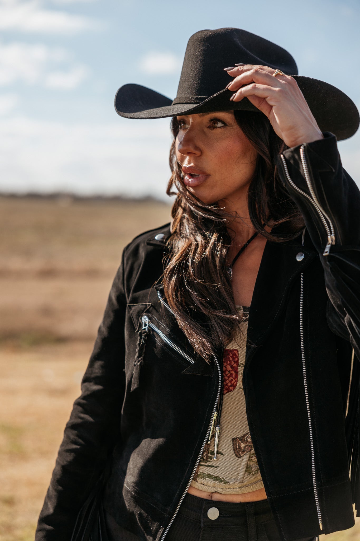 Woman in black cowboy hat and suede western jacket in outdoor boho setting
