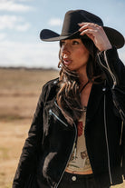 Woman in black cowboy hat and suede western jacket in outdoor boho setting