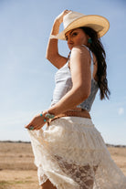 Woman in a white lace skirt, denim top, and cowboy hat in a western boho outdoor setting