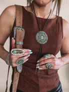 Woman wearing western boho jewelry, turquoise rings, bolo tie necklace, concho belt, brown top
