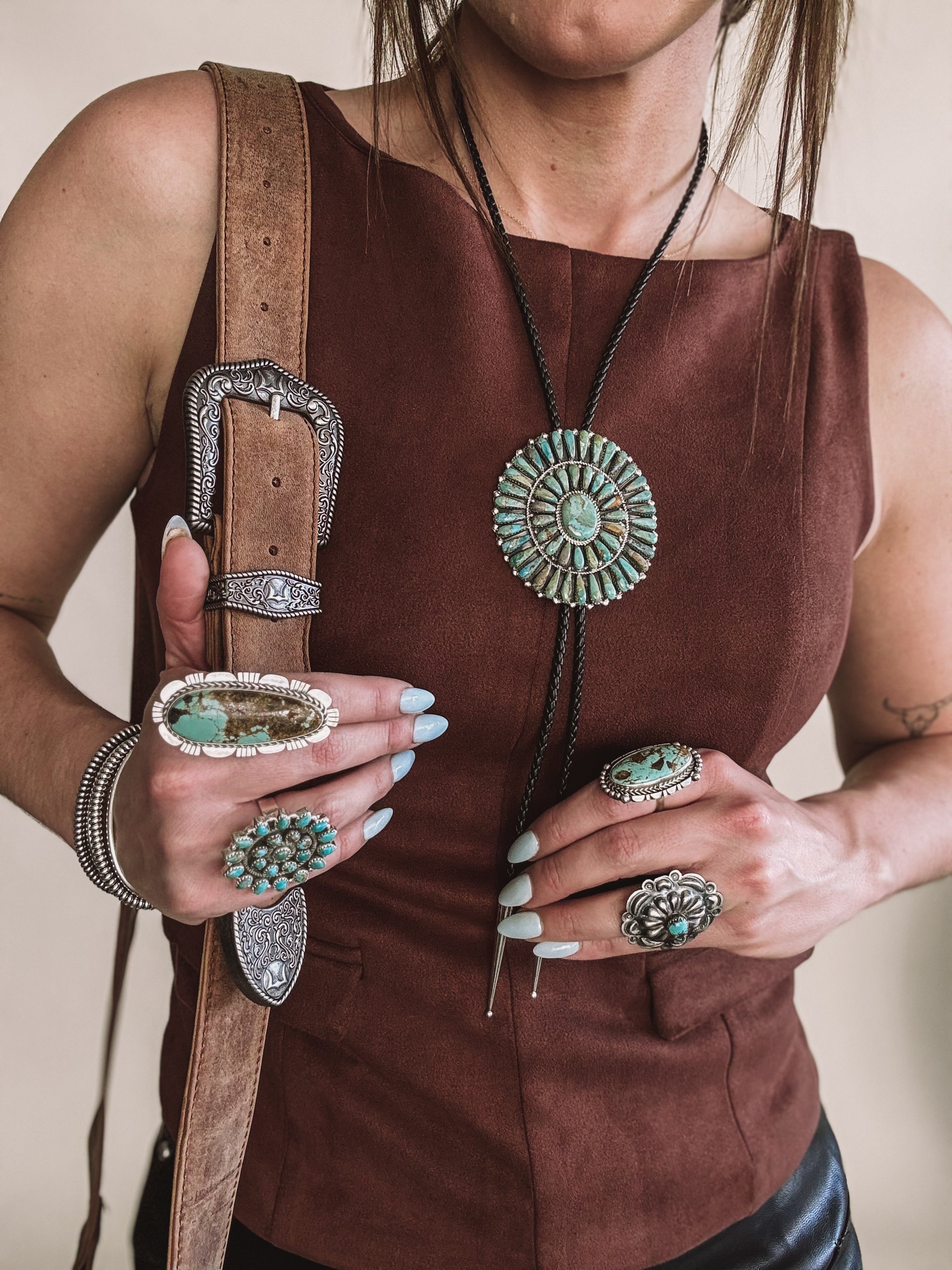 Woman wearing western boho jewelry, turquoise rings, bolo tie necklace, concho belt, brown top