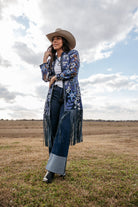 Woman in a western floral fringe jacket, wide-leg jeans, and cowboy hat standing outdoors