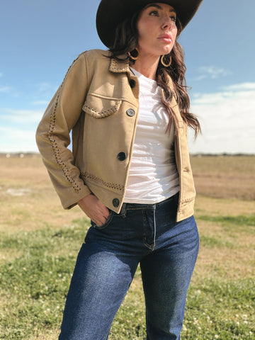 Woman wearing a beige jacket, white shirt, and blue jeans standing in an open field.