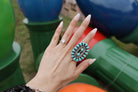 Hand with large turquoise western boho ring and diamond band, colorful background