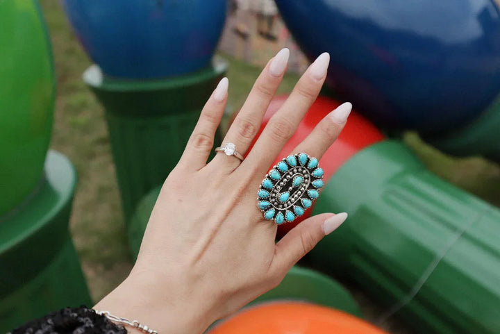 Hand with large turquoise western boho ring and diamond band, colorful background