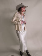 Woman in western cowgirl outfit with beige embroidered jacket, satin skirt, cowboy hat, and boots