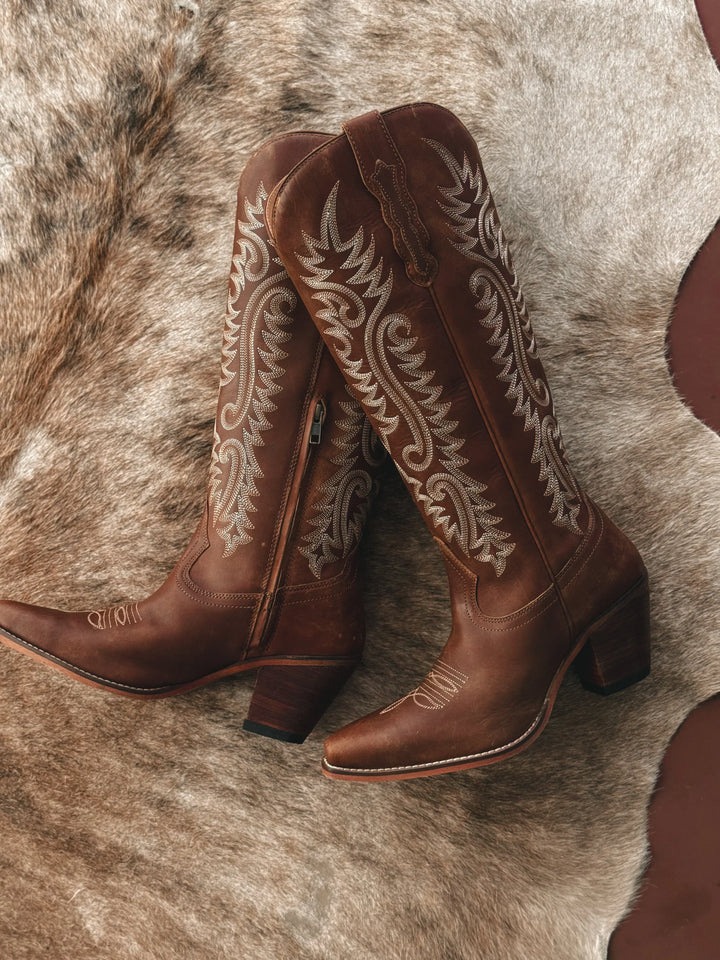Brown cowboy boots with intricate white embroidery on a fur surface