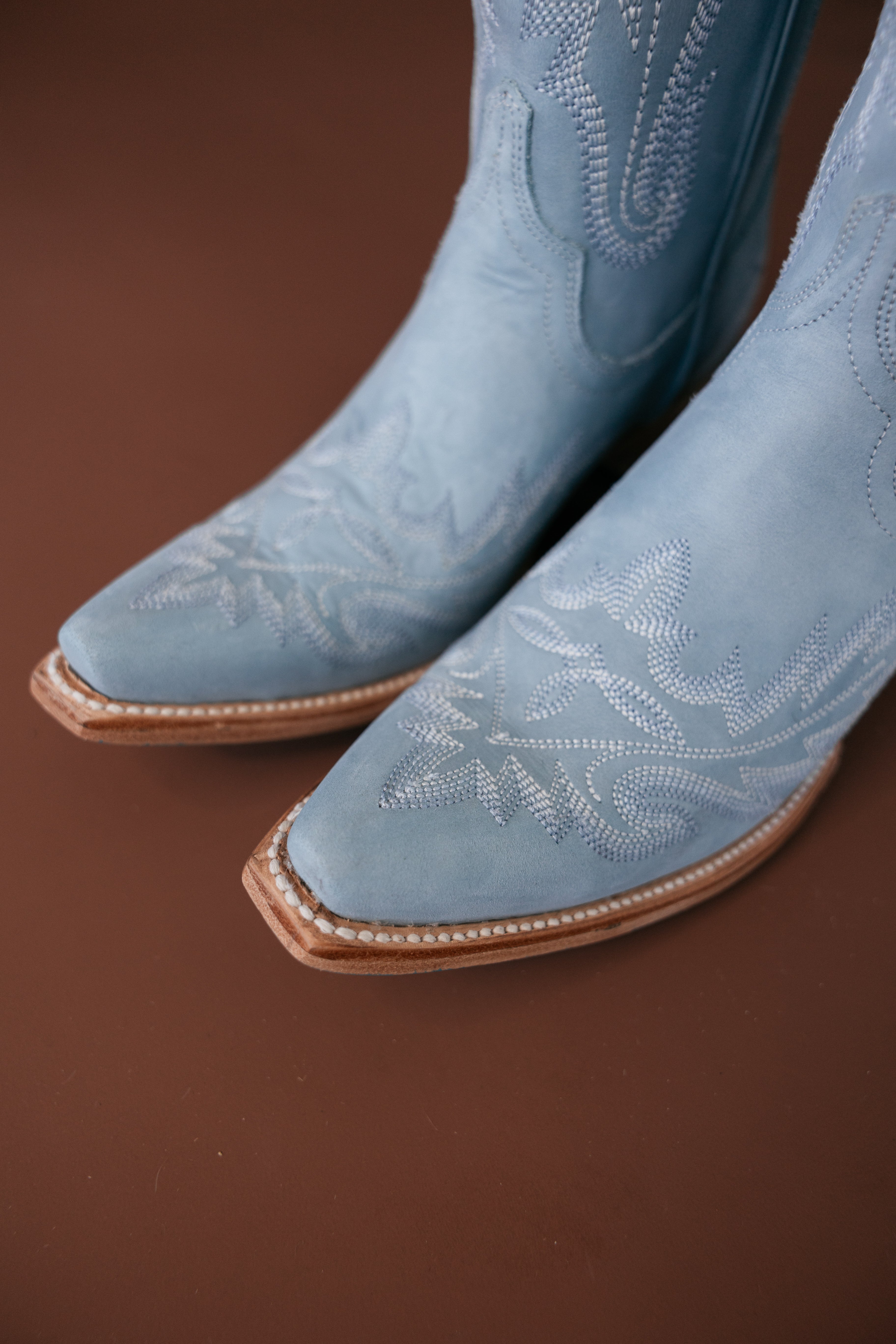 Light blue suede western cowboy boots with decorative stitching on brown background