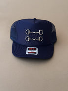 Navy blue western trucker hat with silver horse bit detail and mesh back on beige background.