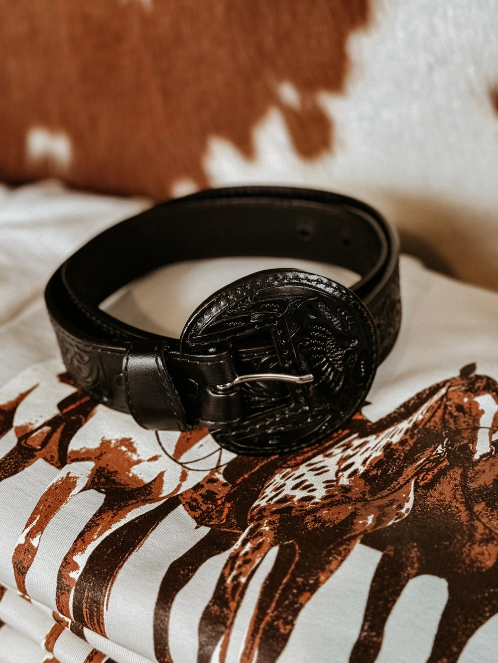 Black tooled western belt with engraved buckle on cow print and horse graphic tee