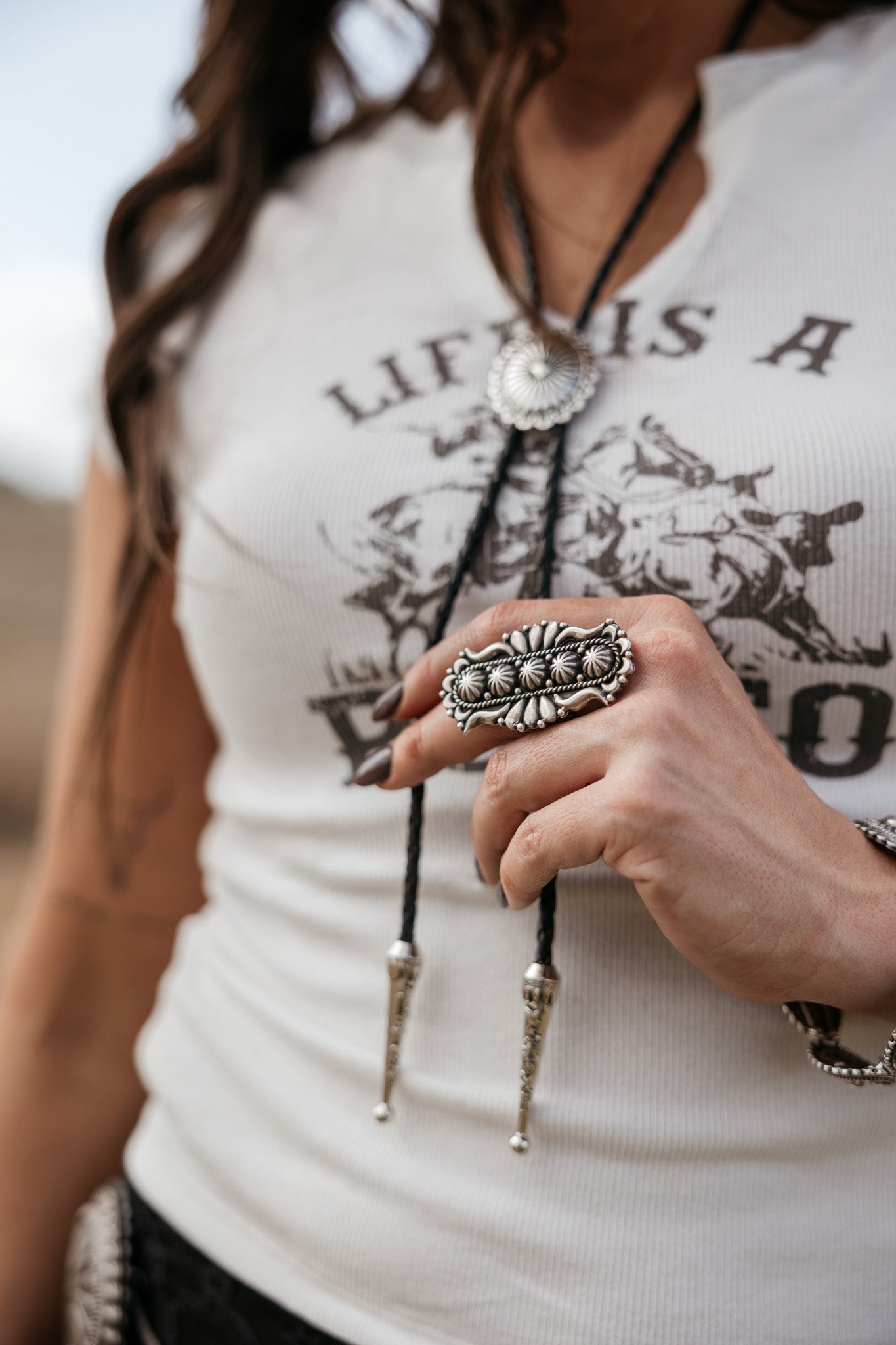 Woman wearing western graphic tee, silver statement ring, and concho bolo tie