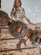 Western boho concho belt with ornate silver buckles resting on a magazine featuring a woman in cowgirl boots and western outfit outdoors.