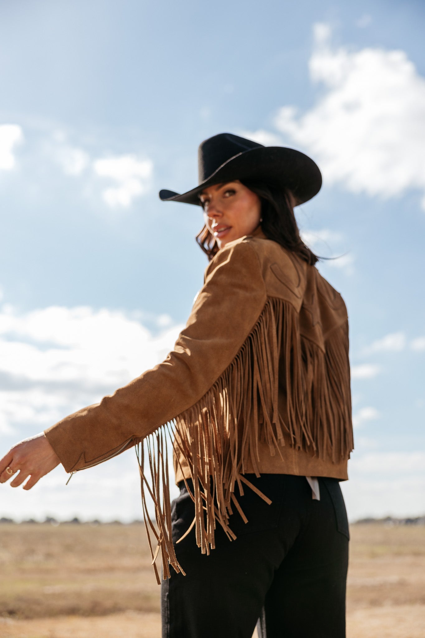 Woman in suede fringe western jacket and black cowboy hat outdoors