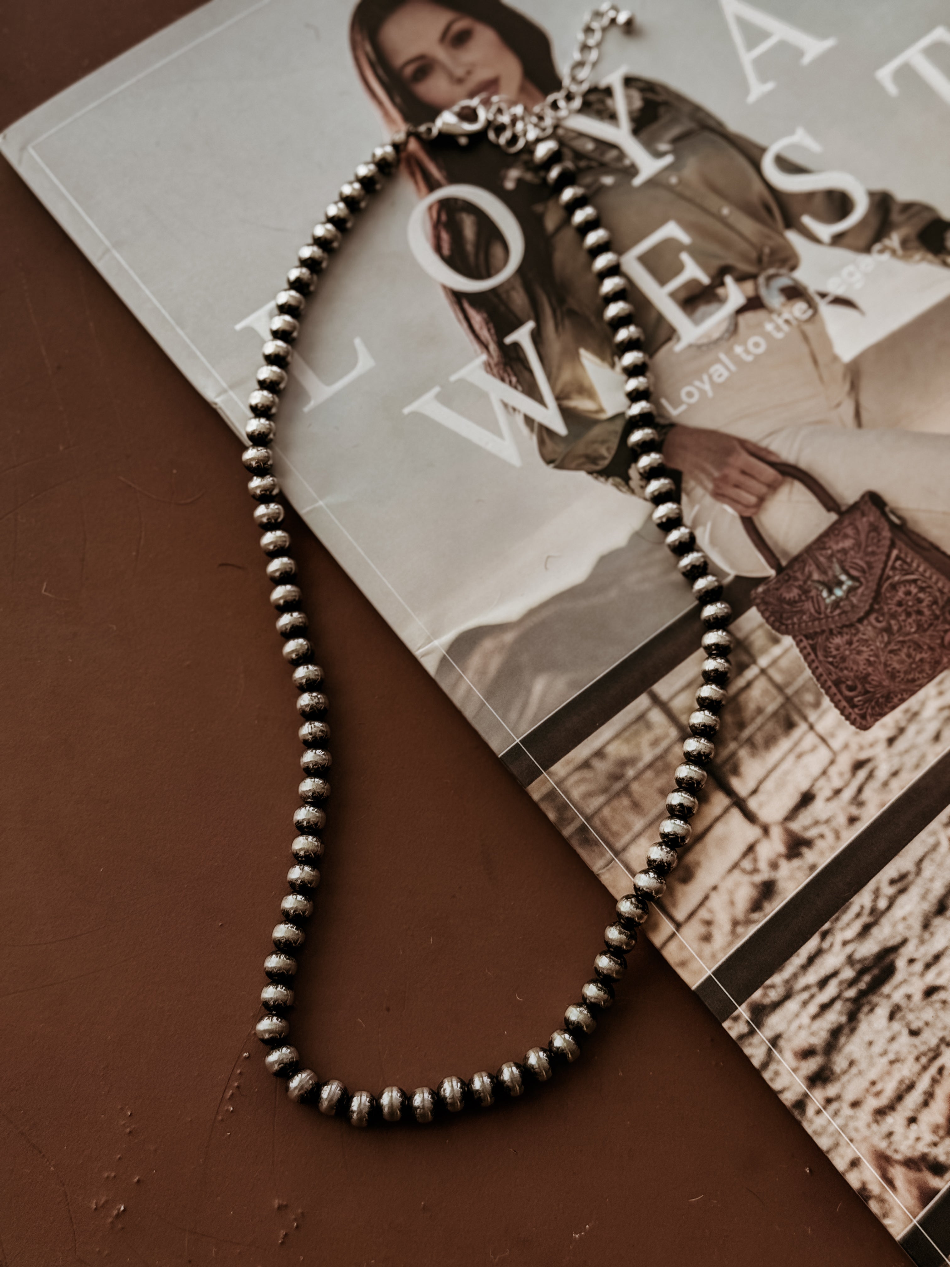 Silver western bead necklace on brown table with cowgirl magazine