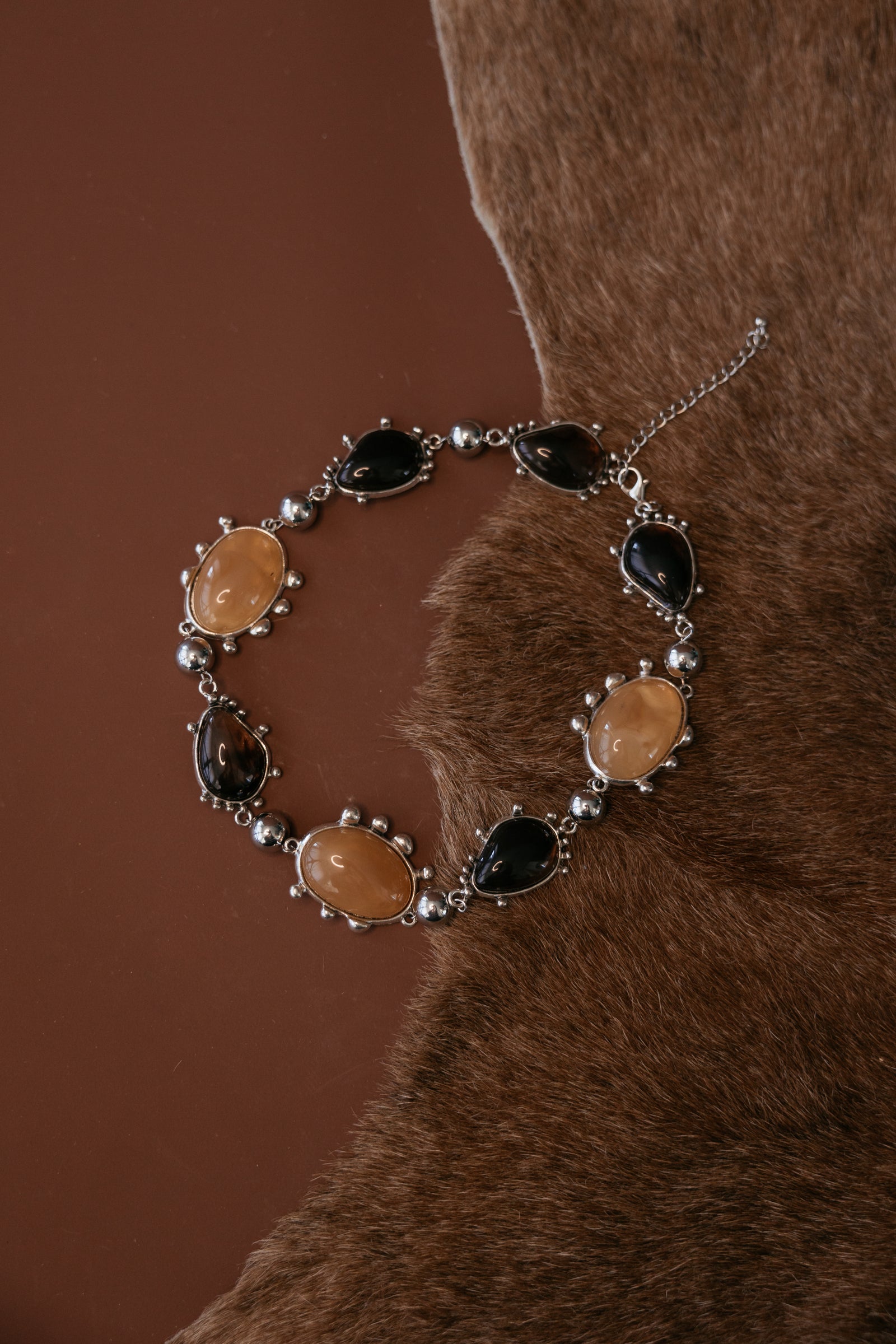 Chunky metal collar necklace with bezel‑set resin cabochon gemstones and a silver rhodium antique finish.