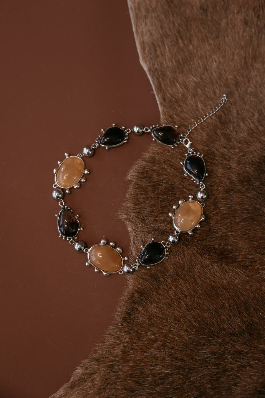 Chunky metal collar necklace with bezel‑set resin cabochon gemstones and a silver rhodium antique finish.