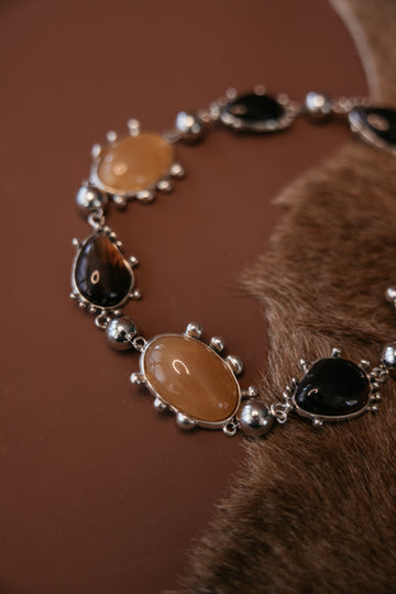 Chunky metal collar necklace with bezel‑set resin cabochon gemstones and a silver rhodium antique finish. Close up.