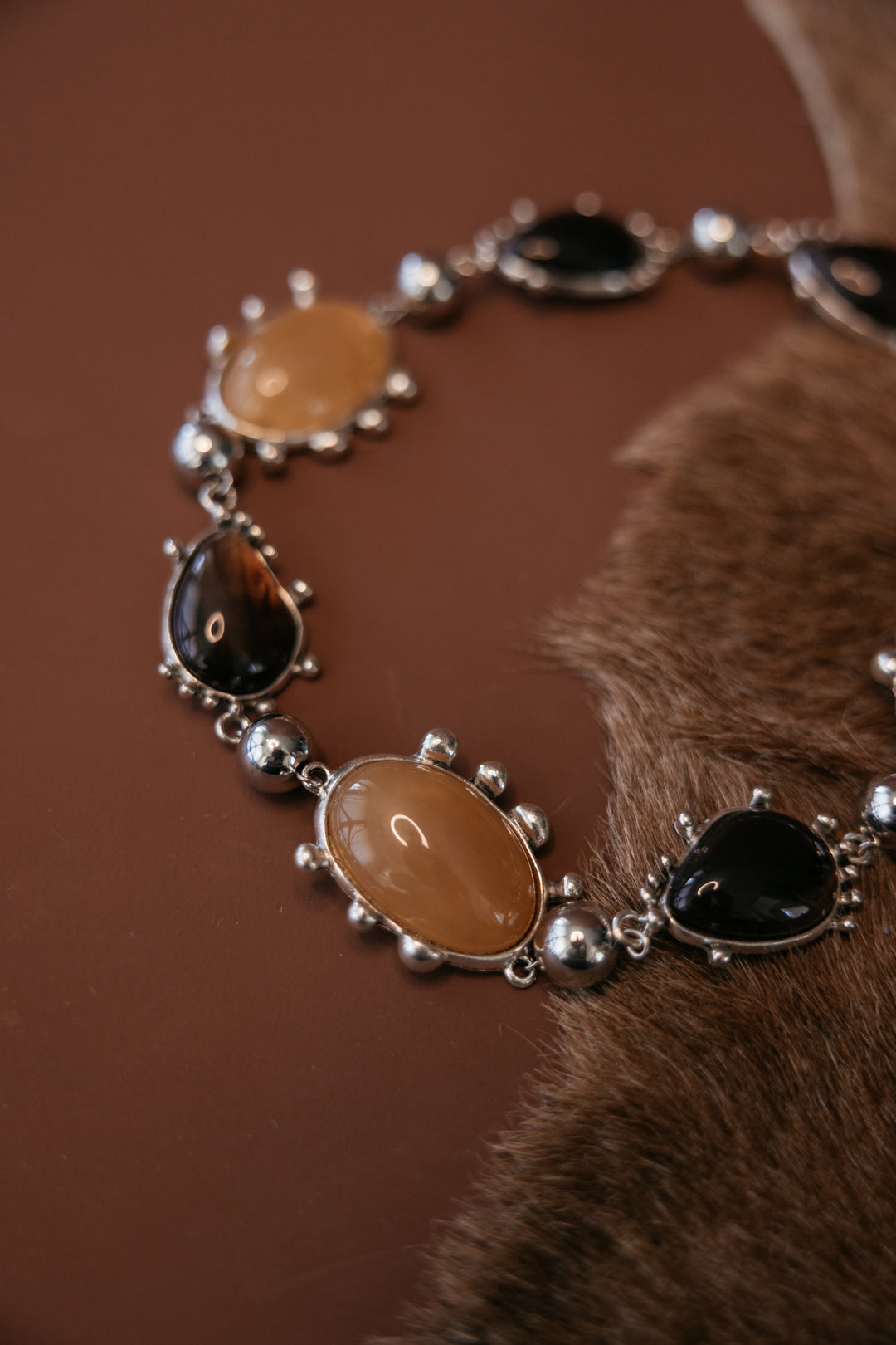 Chunky metal collar necklace with bezel‑set resin cabochon gemstones and a silver rhodium antique finish. Close up.