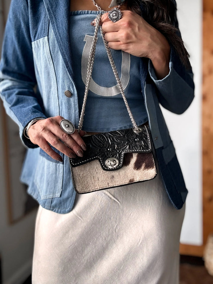 Person holding a decorative cowhide handbag with a blue jacket and white pants.