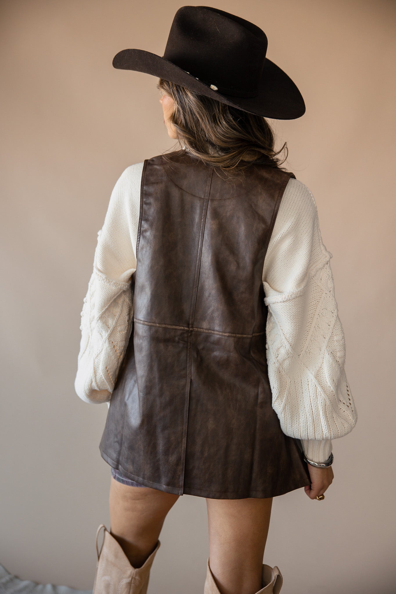 Woman in brown faux leather dress, cream knit sleeves, cowboy hat and boots, western style