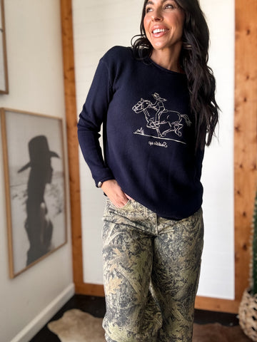 Woman wearing a navy sweatshirt with a graphic design, standing indoors.