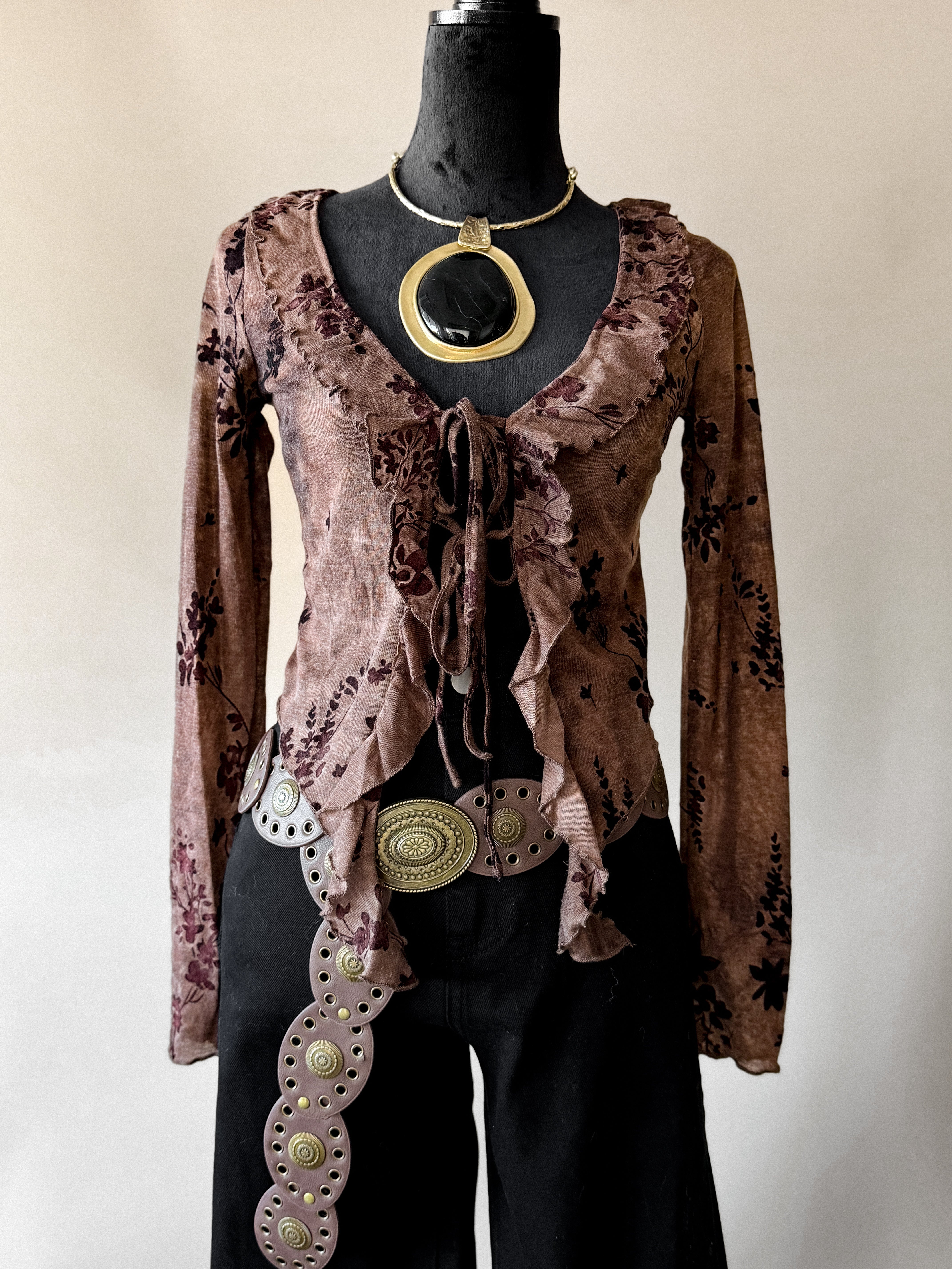 Mannequin wearing a brown patterned top with decorative belt and necklace on a plain background